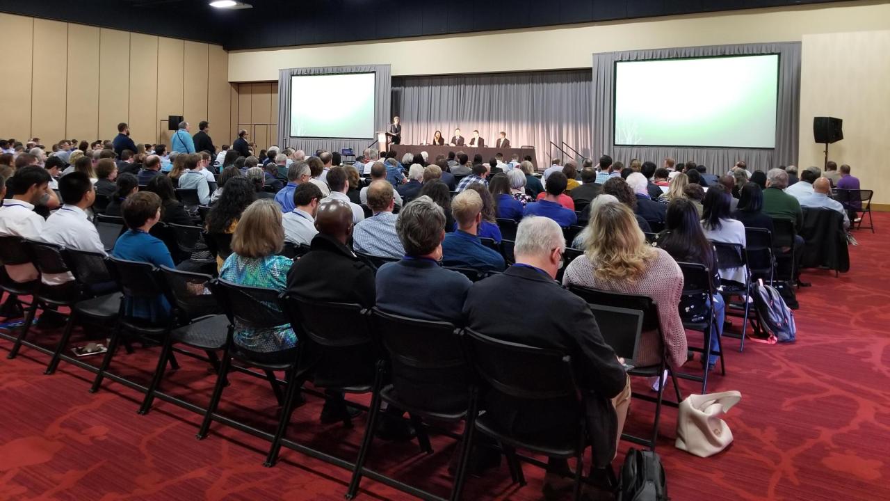 Image: a large group of people sit in a conference room for ASIC.