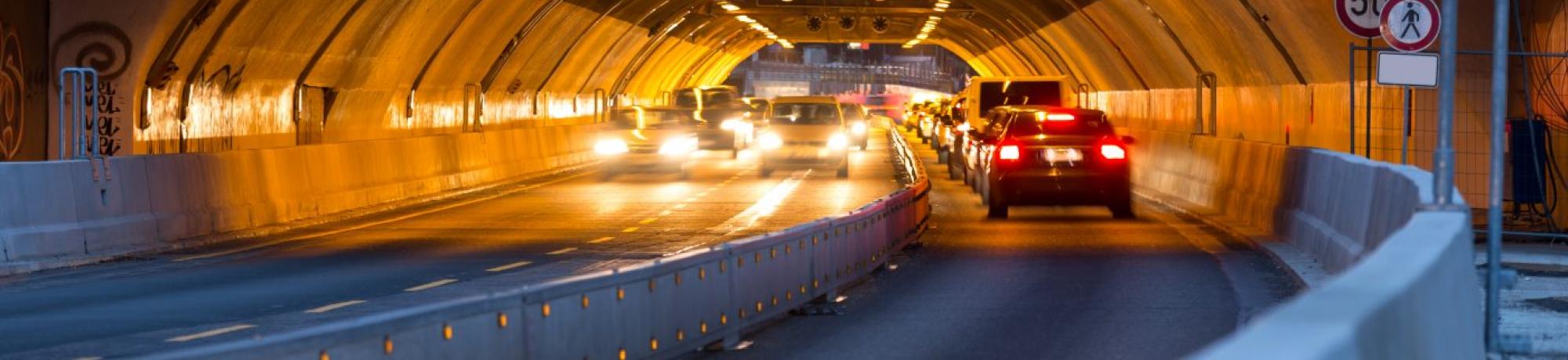 Image: a vehicular tunnel with cars driving through.